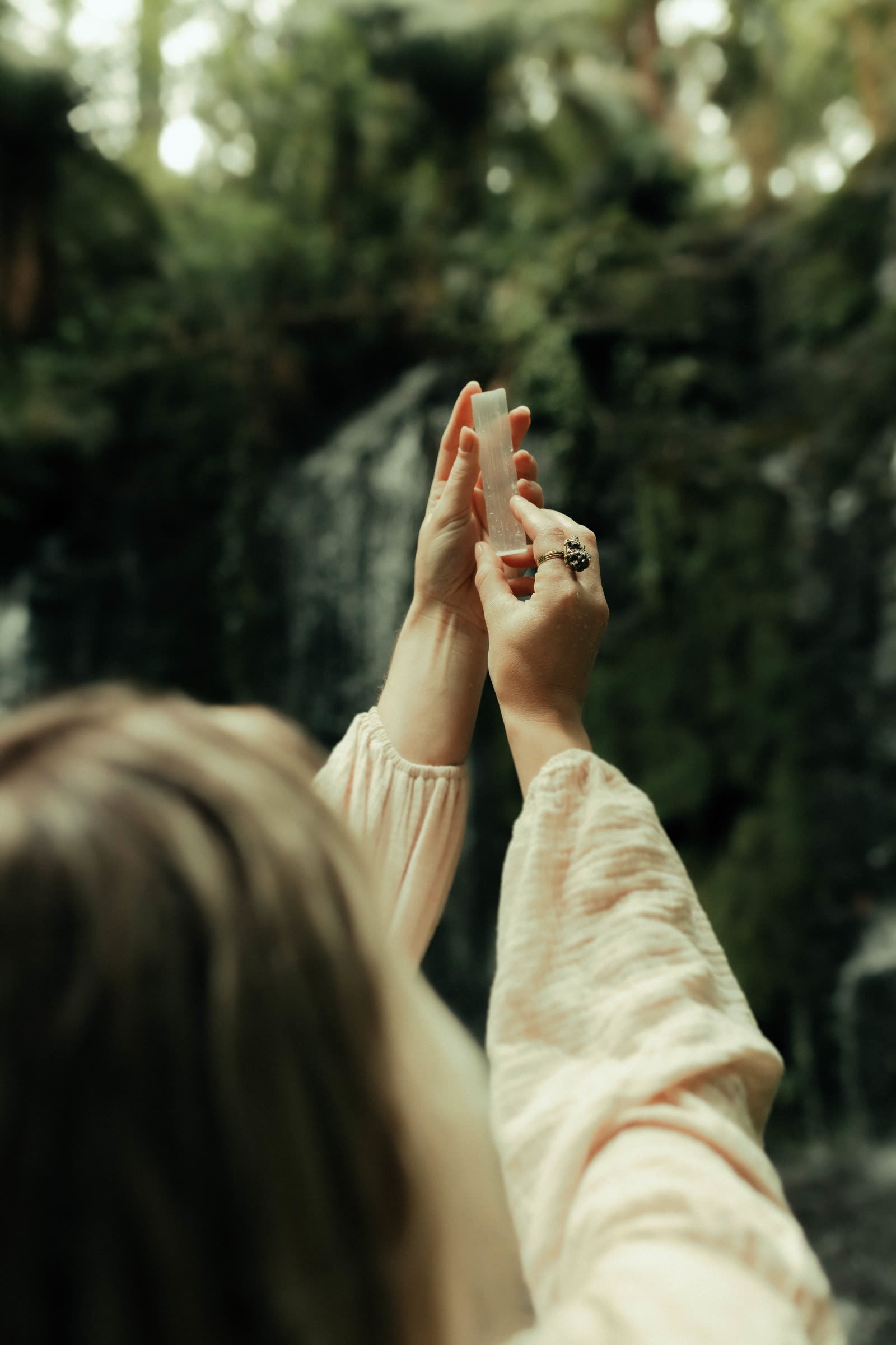 Mãos com cristal diante da cachoeira